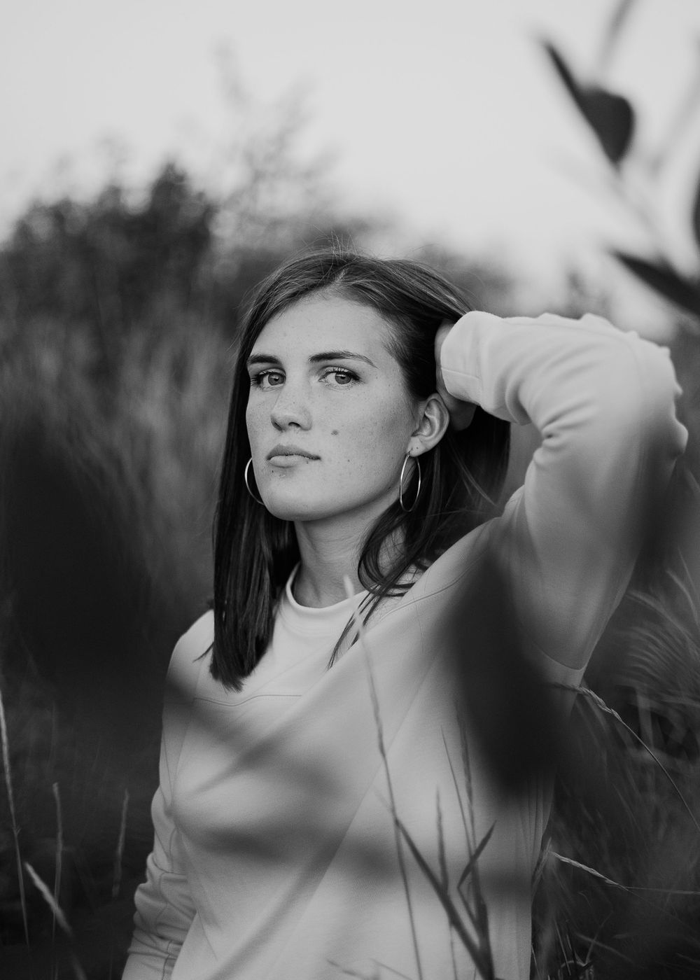 Black and white portrait of person with long dark hair in natural setting.