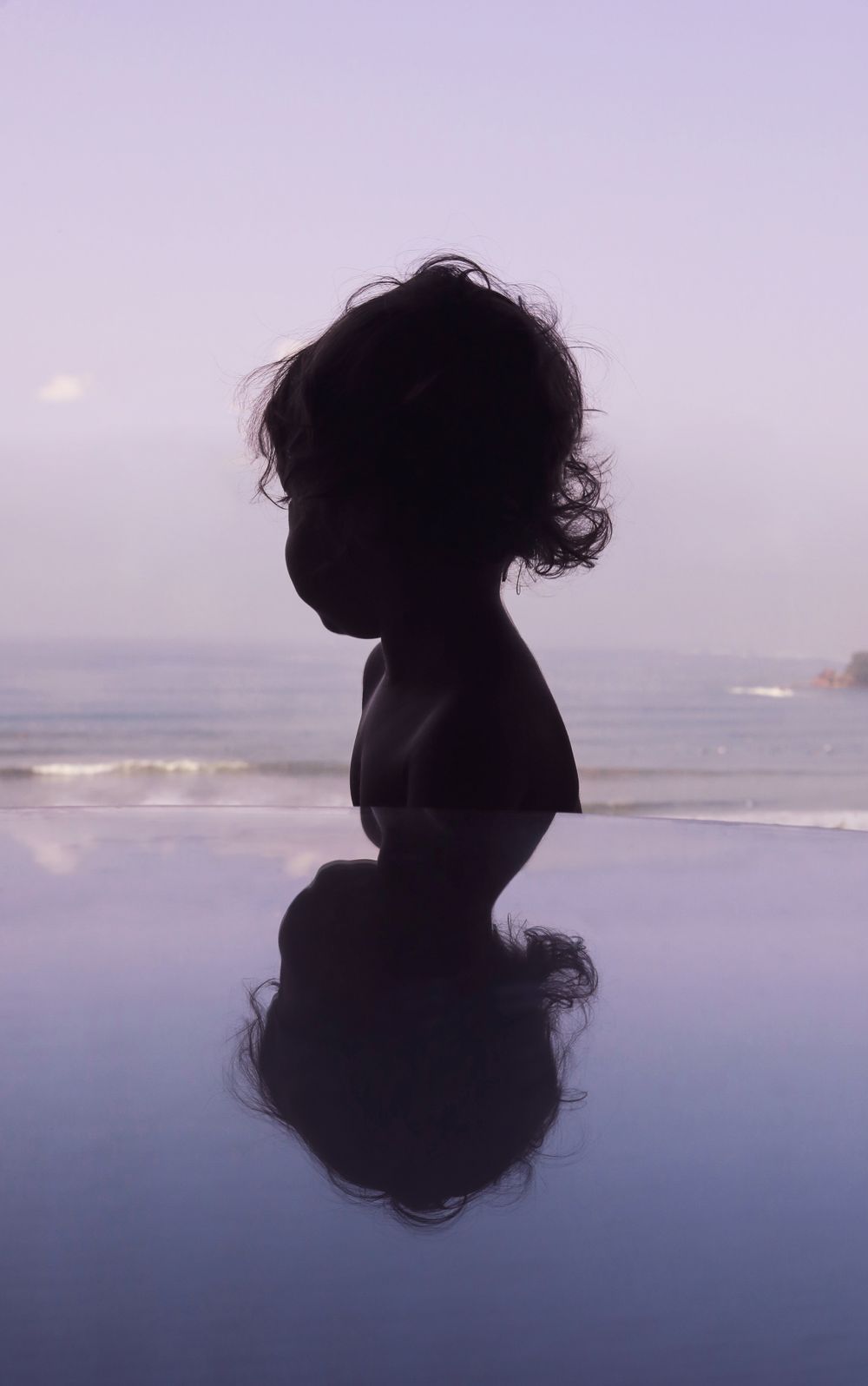 Silhouette reflected in still water against purple twilight sky at beach.