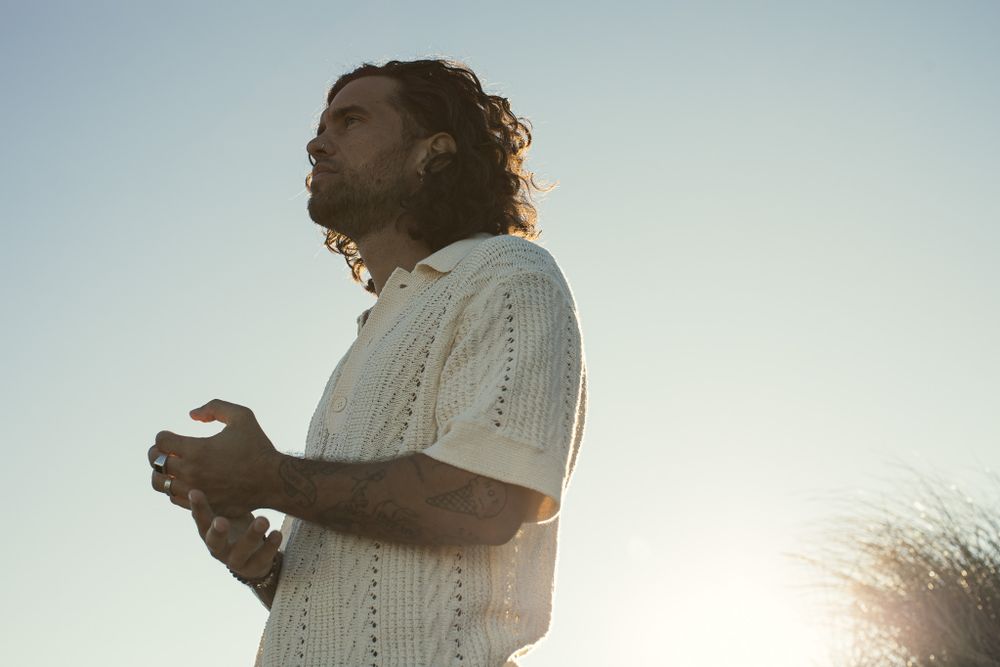 A silhouetted figure stands in a white sweater against a bright sunset sky.