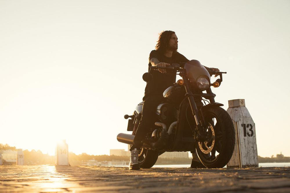 Silhouettes of people with motorcycles at sunset against a bright horizon.