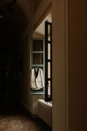 A white suit jacket hangs in a sunlit window frame against a dark hallway interior.