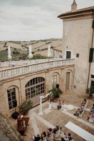 Elegant outdoor wedding ceremony setup at a historic Italian villa with stone balustrades overlooking rolling hills.