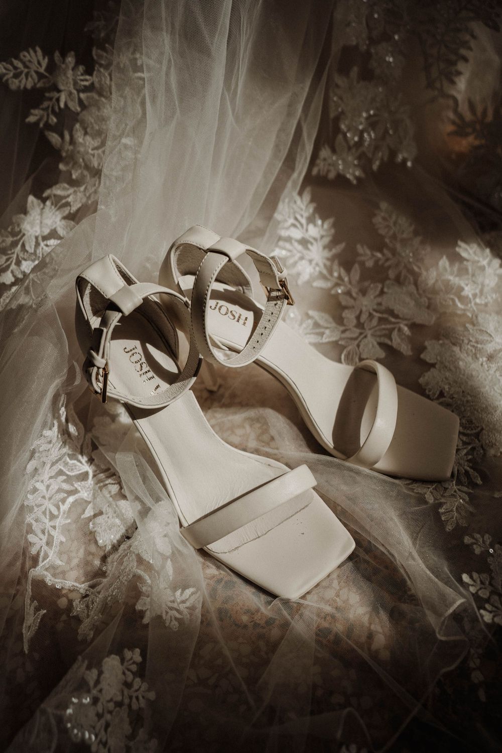 Elegant white bridal sandals with straps displayed on lace fabric.