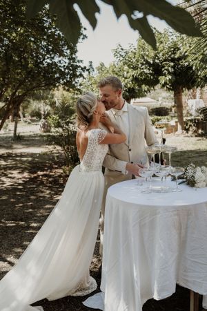 Newlyweds sharing intimate moment by outdoor reception table in sunny garden setting.