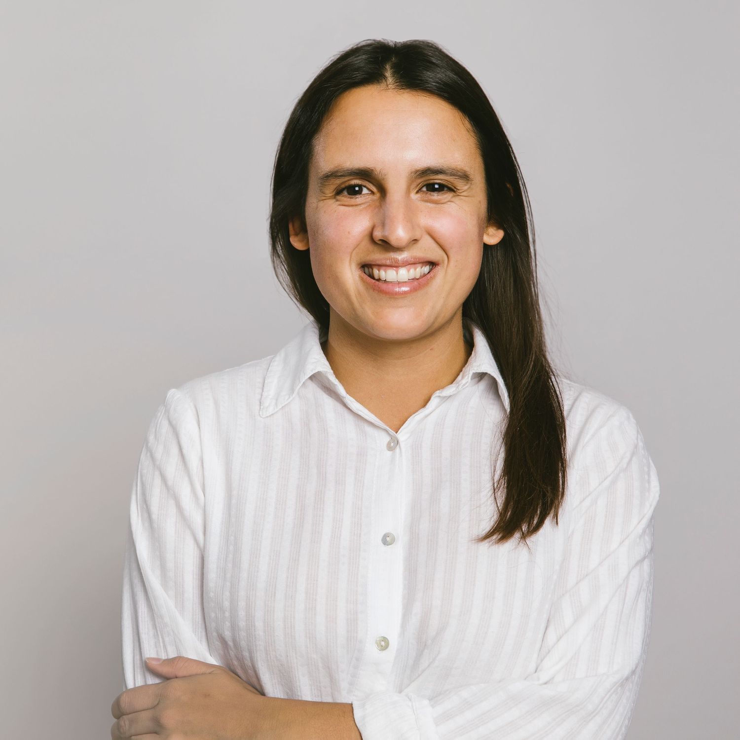 A professional headshot of a person with long dark hair wearing a white striped button-down shirt.