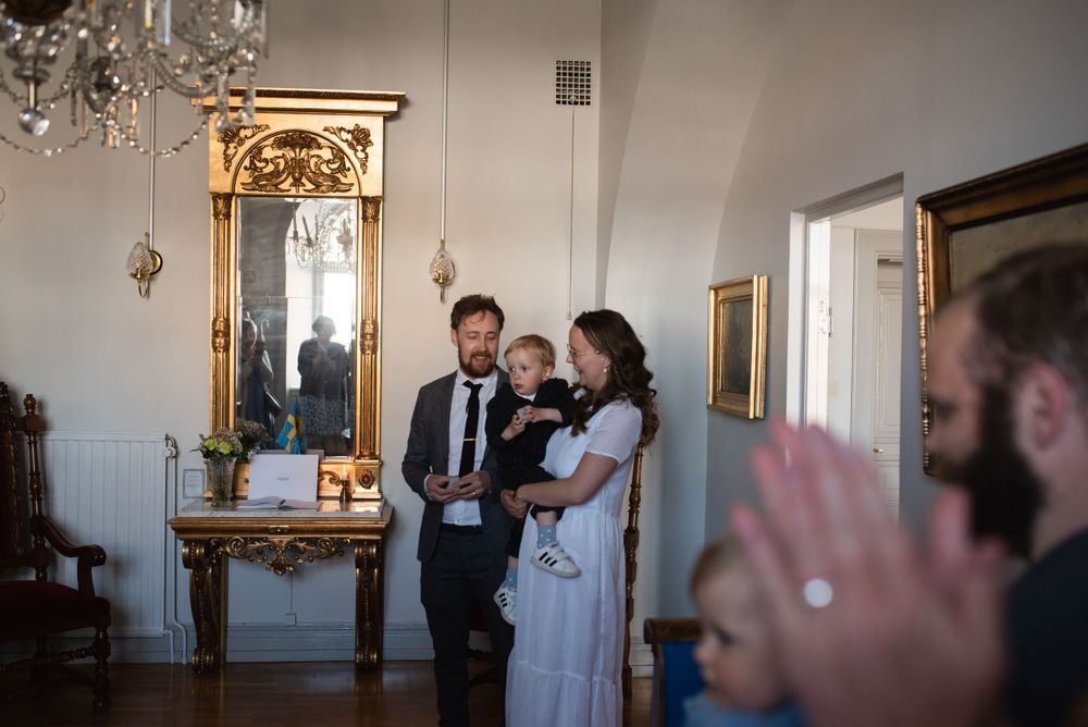 Indoor ceremony taking place in an elegant room with ornate gold mirror and chandelier.