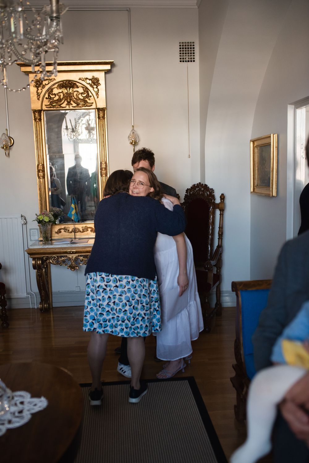 Group sharing a moment in front of an ornate gold mirror in a formal setting.