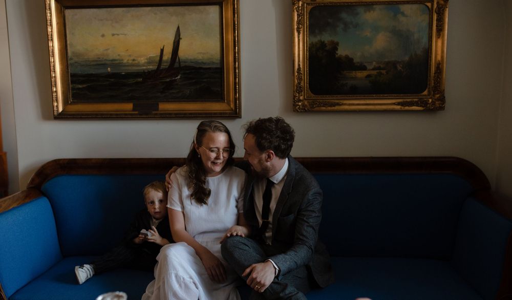Intimate moment shared on blue sofa beneath framed landscape paintings.