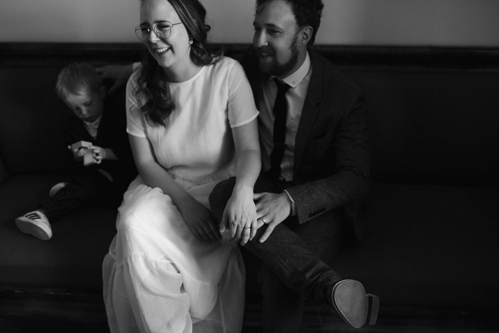 A black and white photo captures a joyful moment between a couple seated on a couch.