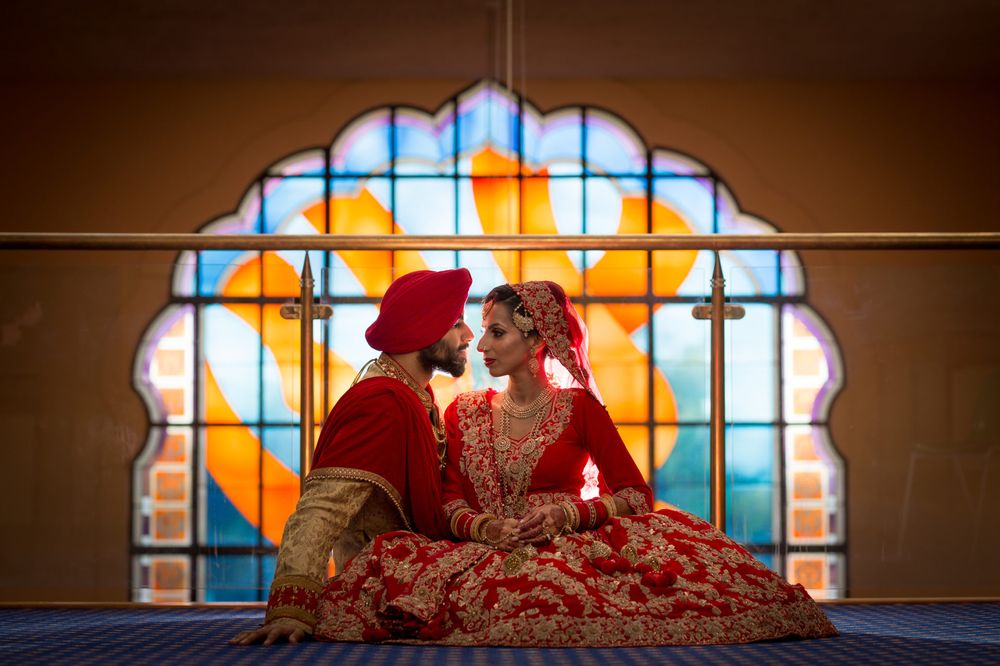 Couple in traditional Indian wedding attire posed before colorful stained glass window.