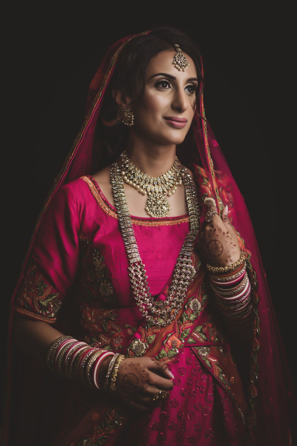 Traditional Indian bride wearing ornate red lehenga and jewelry against dark background.