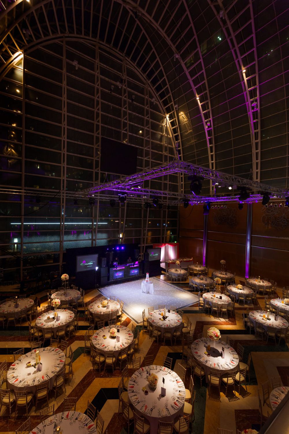Elegant wedding reception venue with clock-themed table settings under purple-lit arched ceiling.