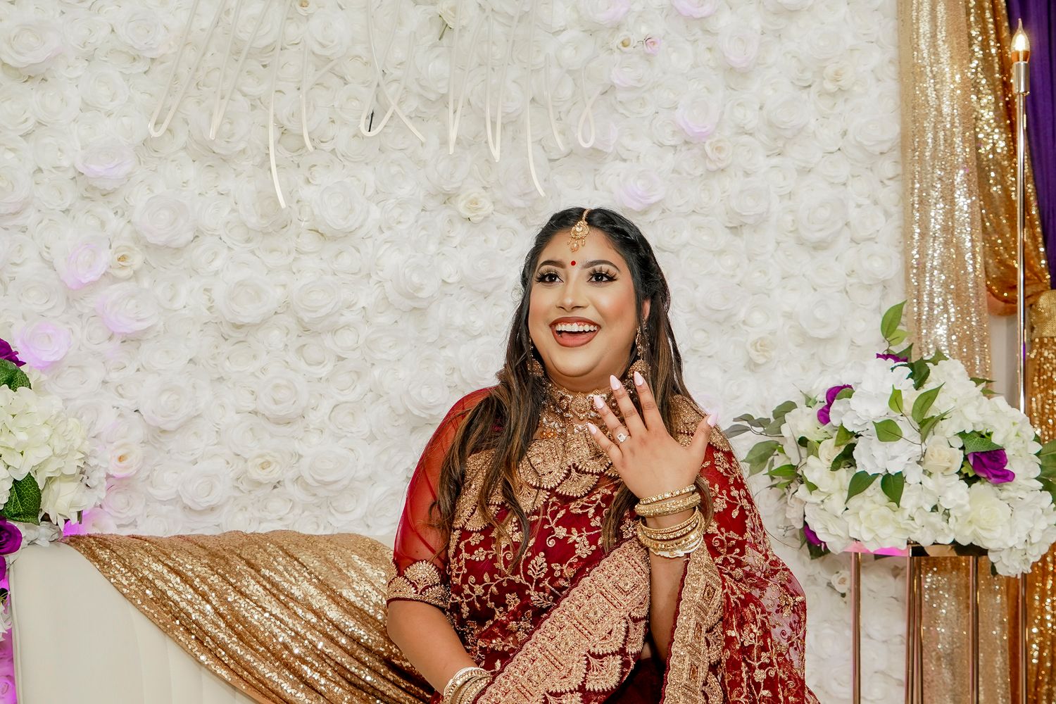 Bride in ornate red lehenga and jewelry smiles during Indian wedding celebration.