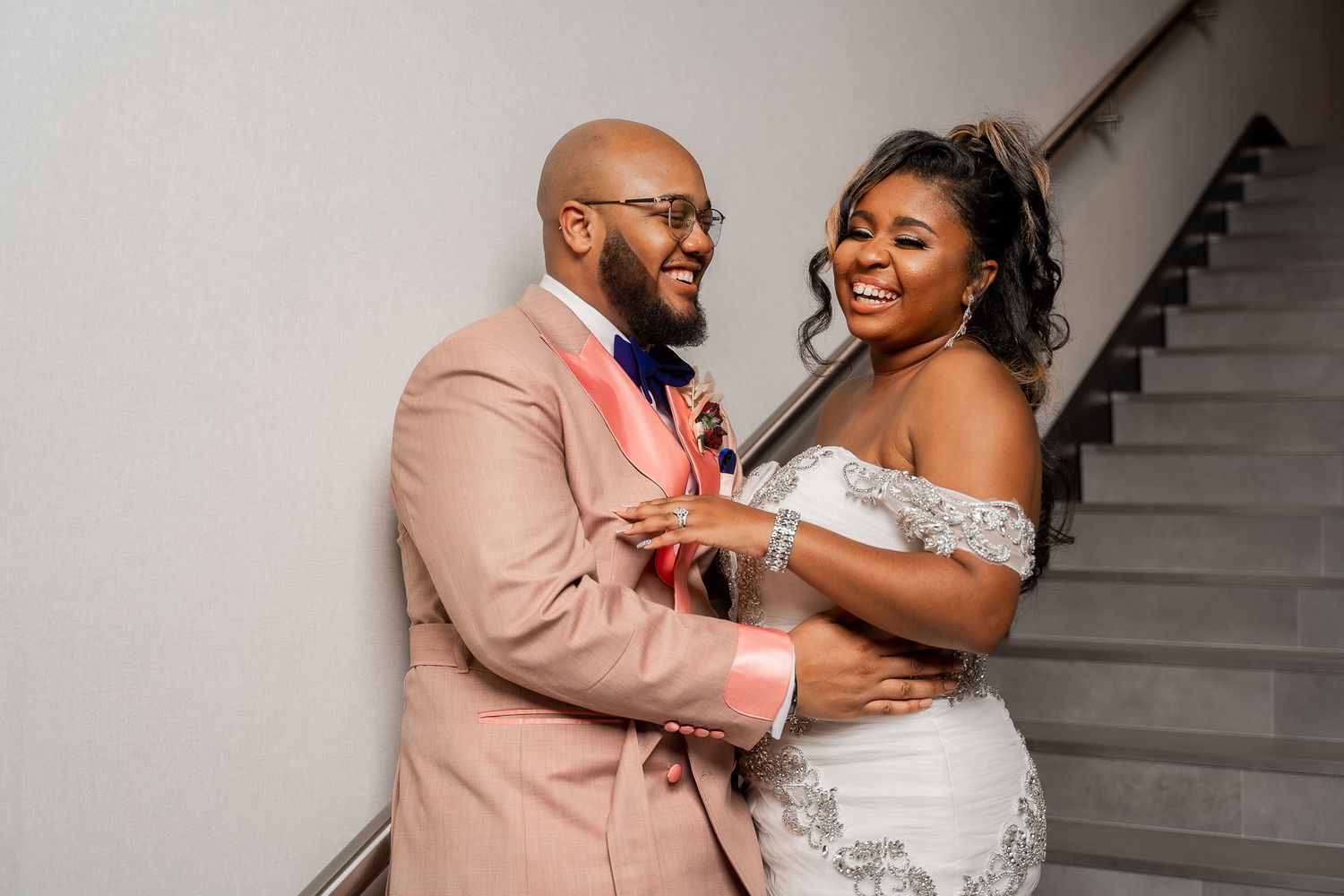 A joyful wedding moment captured on stairs with the couple in blush pink and white attire.