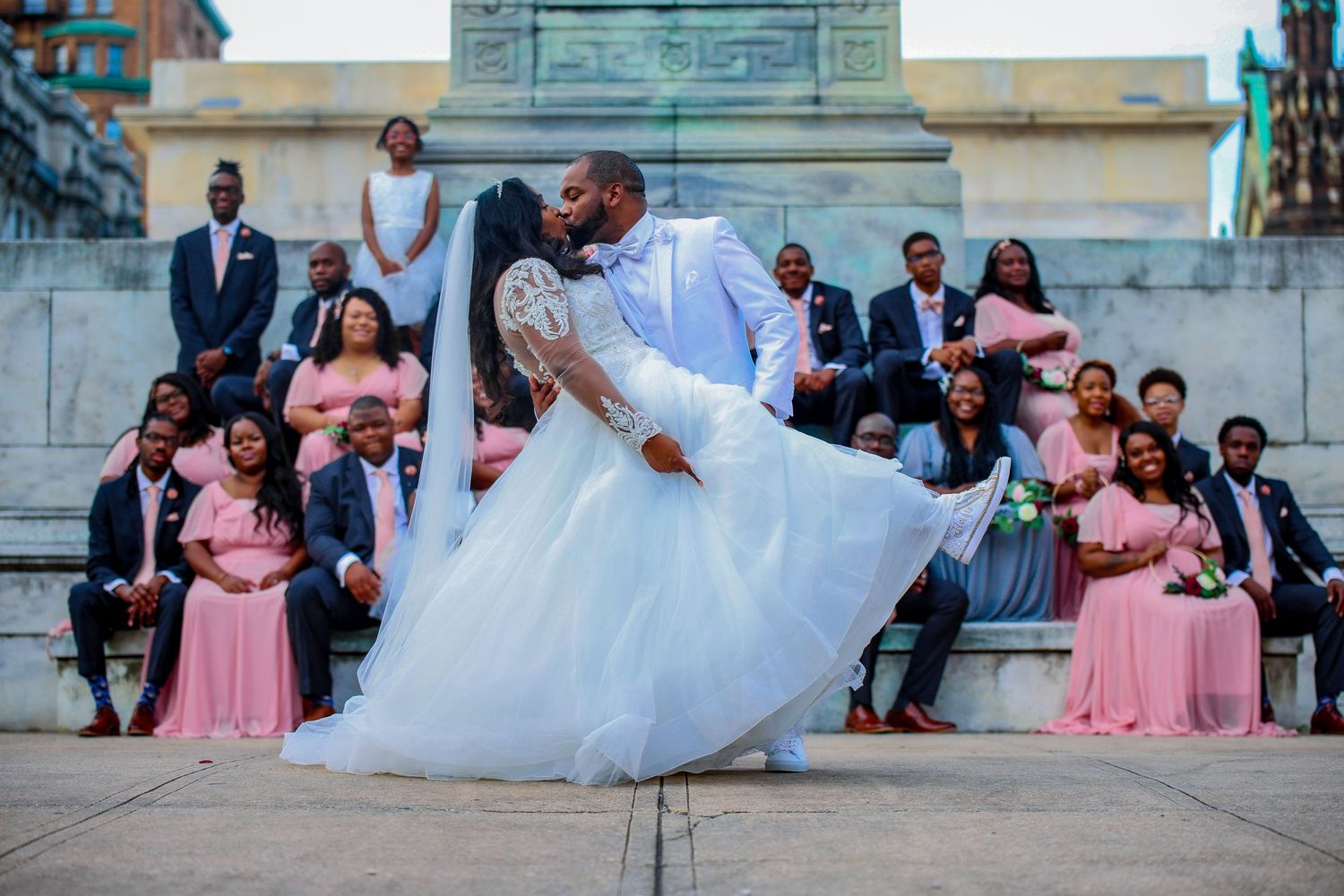 A romantic dip during a wedding dance with bridesmaids in pink dresses watching from stone steps.