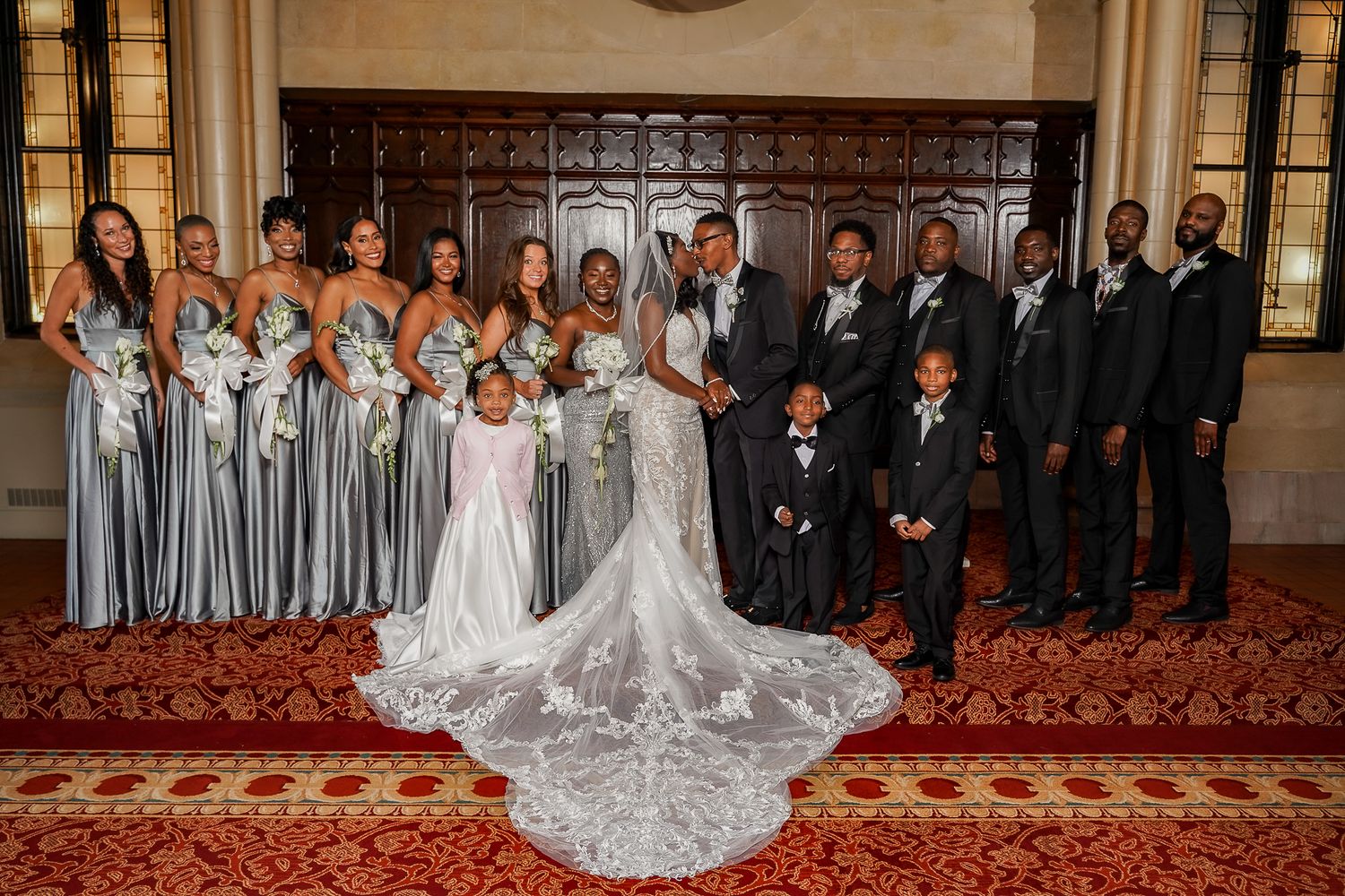 Wedding party portrait with bridesmaids in gray dresses and groomsmen in black tuxedos.