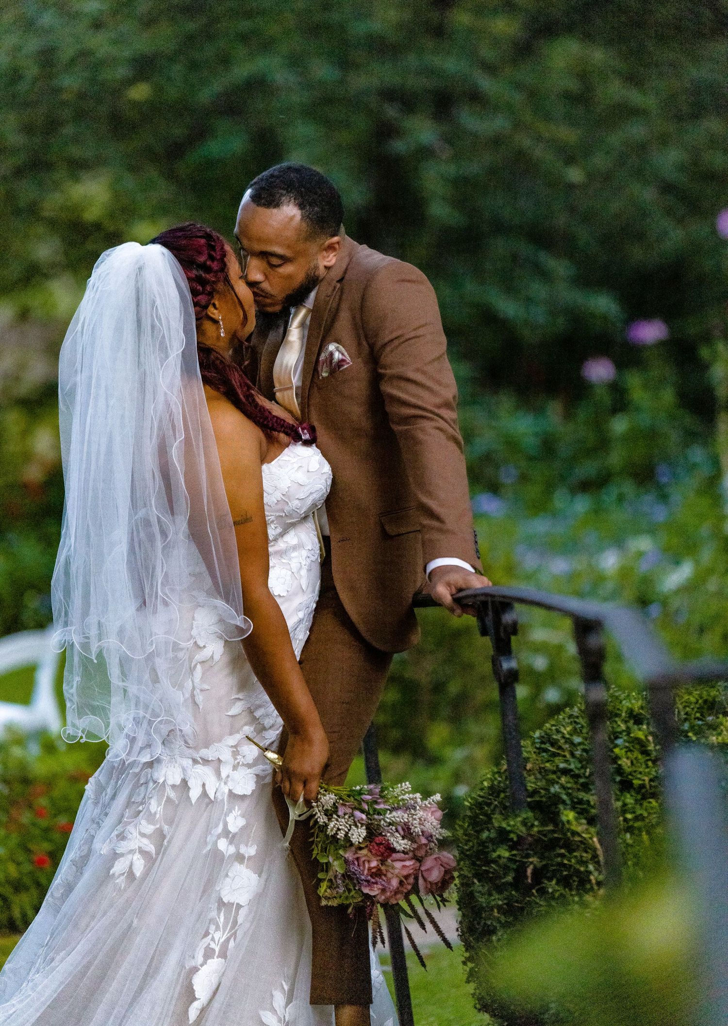 A romantic wedding couple shares an intimate moment in a garden setting with lush greenery.