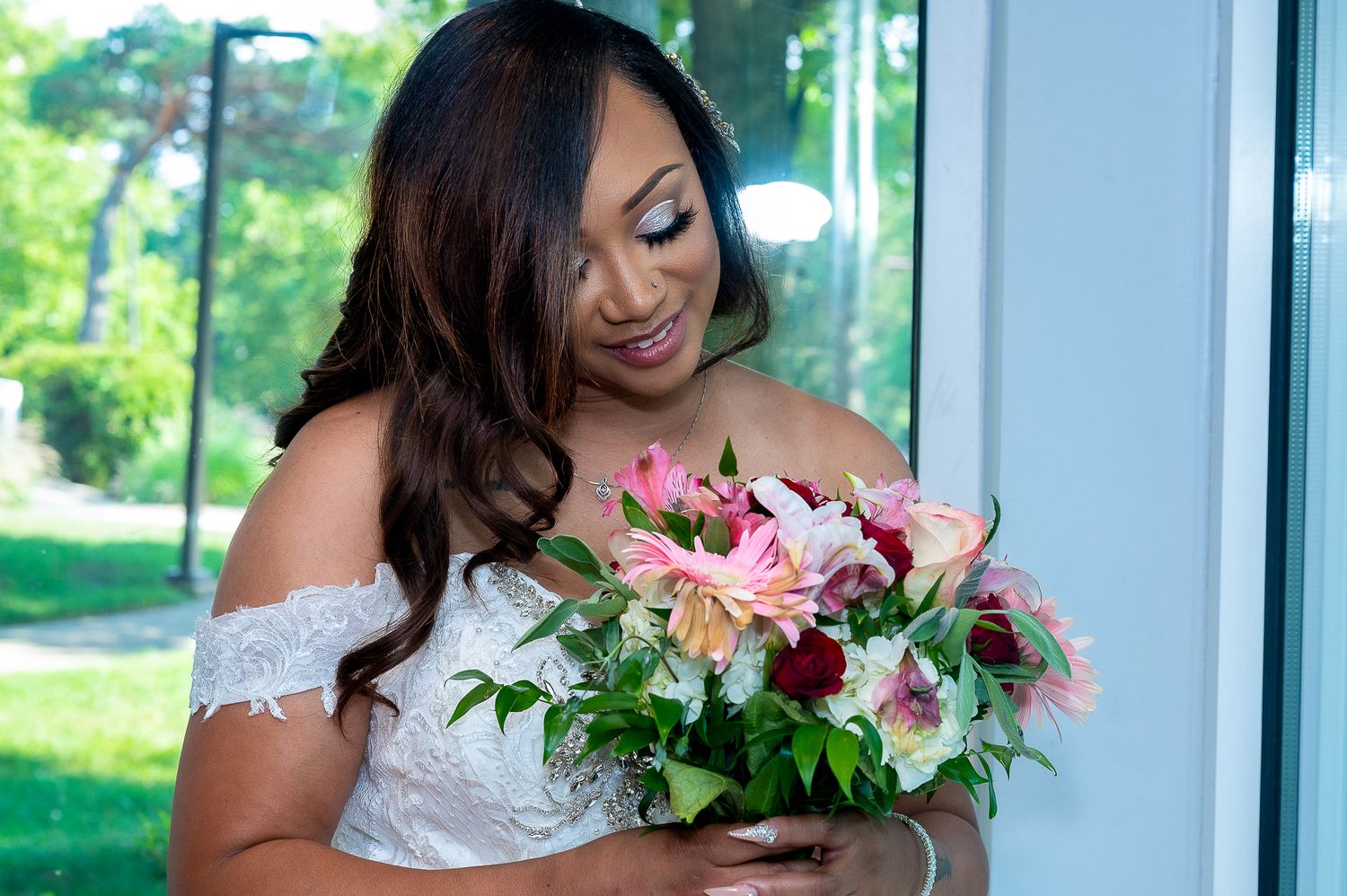 Elegant white wedding dress with lace details and pink floral bouquet in natural lighting.