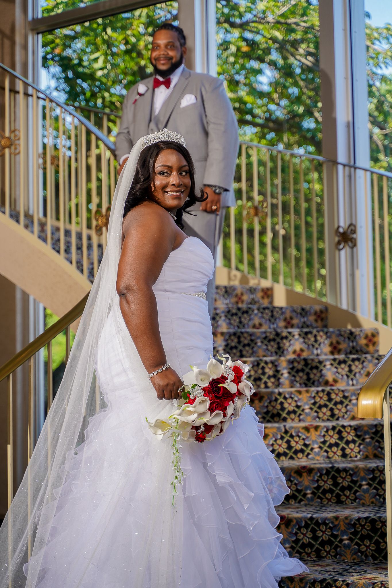 Bride holding a red and white bouquet while posing on decorative tiled stairs.