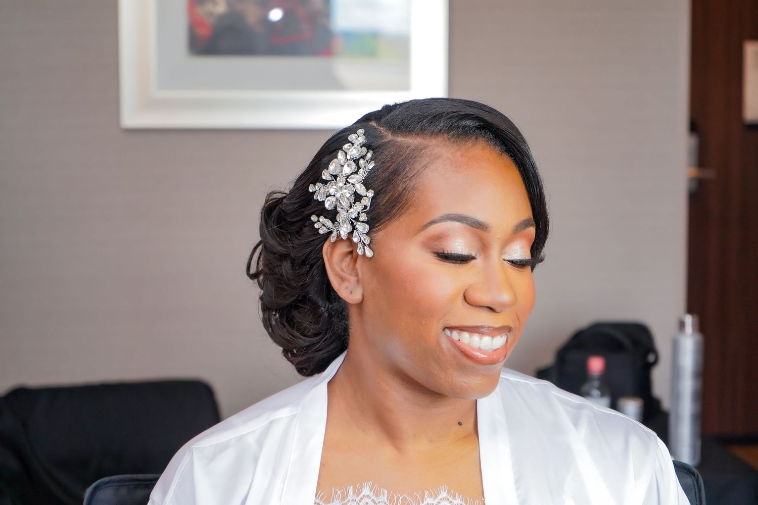 Bride in white robe with elegant hair and makeup during wedding preparations.
