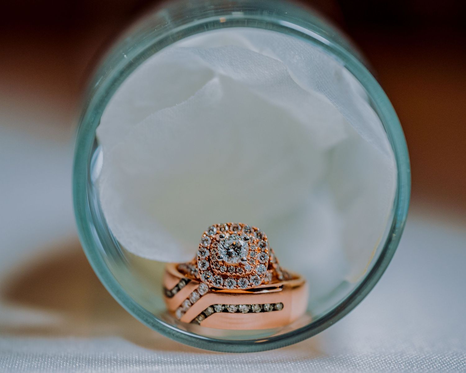 Rose gold engagement ring with diamond details displayed on aqua glass surface.