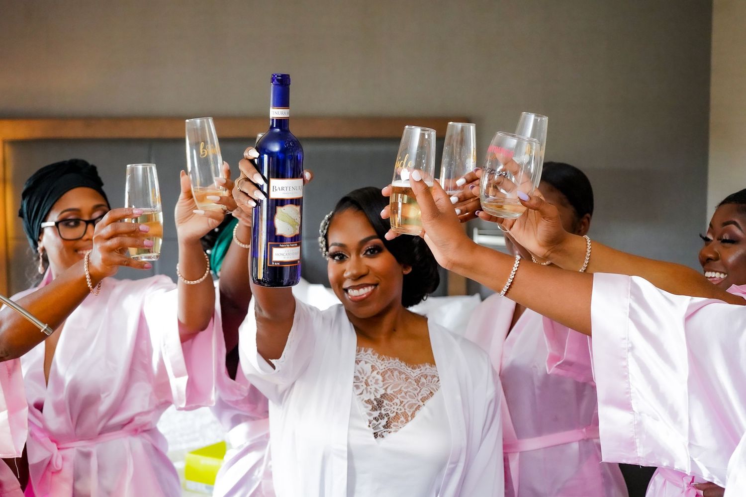 Wedding party raising glasses in a celebratory toast wearing matching pink robes.