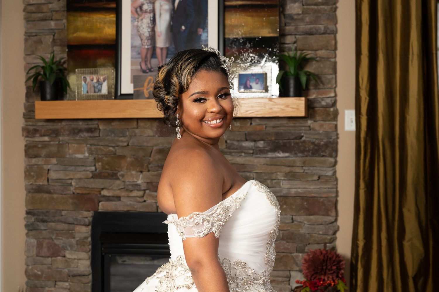 A stunning bride in an off-shoulder white ballgown poses in front of a stone fireplace.