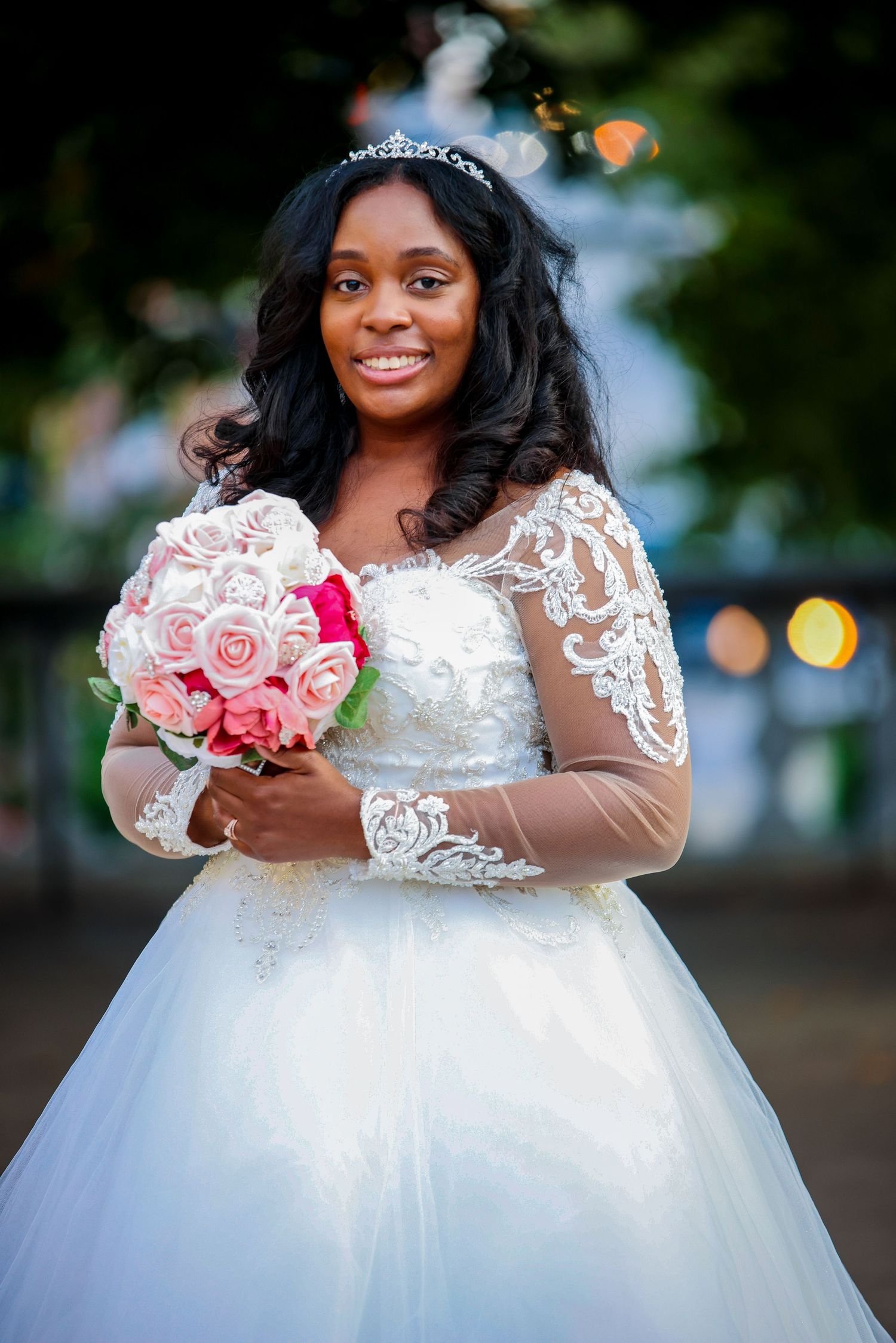 A bride in a white lace gown holds a pink rose bouquet.