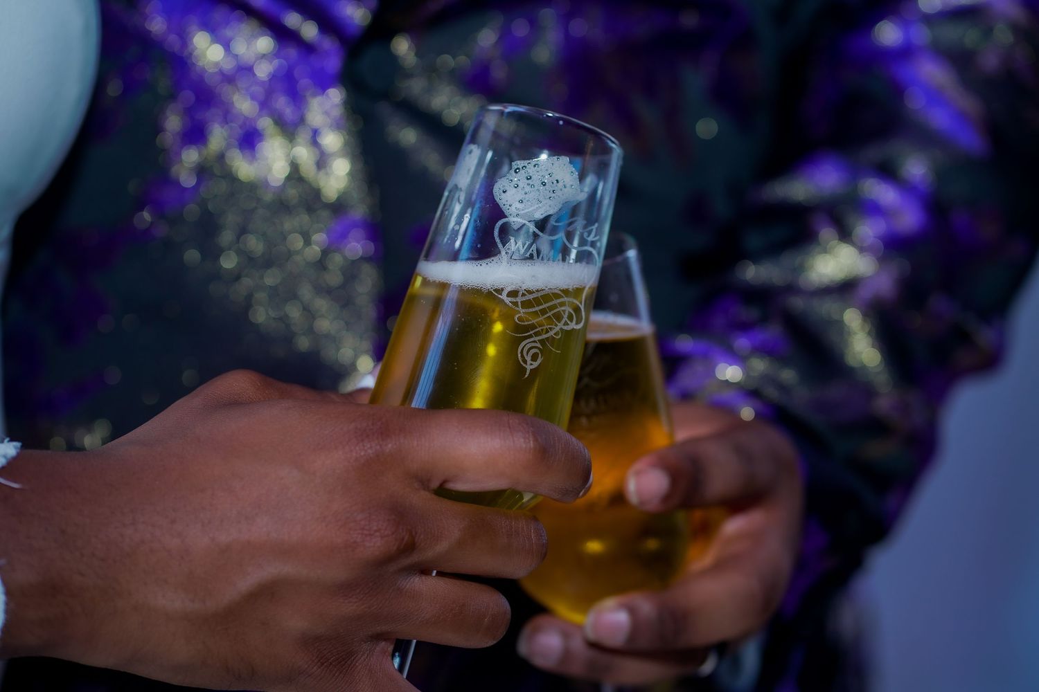 Wedding guests toasting with drinks in purple ambient lighting.