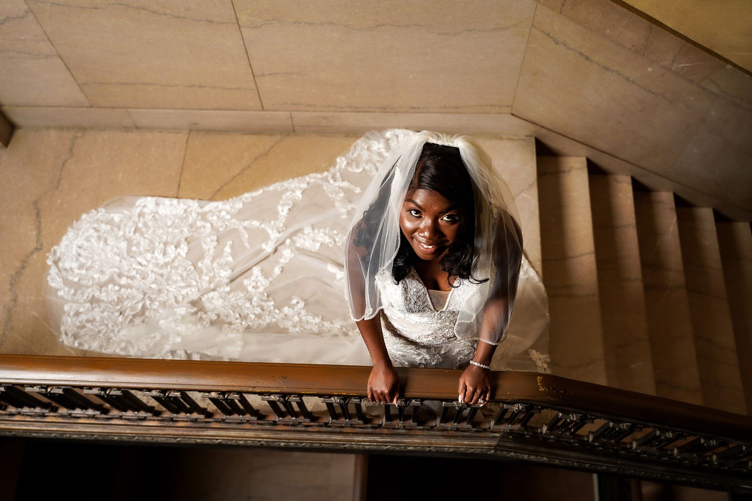 Wedding party poses on grand marble staircase with ornate architectural details.