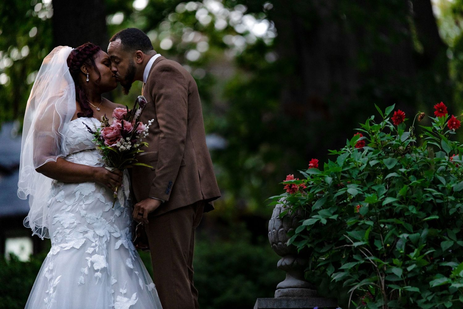 Newlyweds embrace tenderly in a garden surrounded by blooming flowers and natural scenery.
