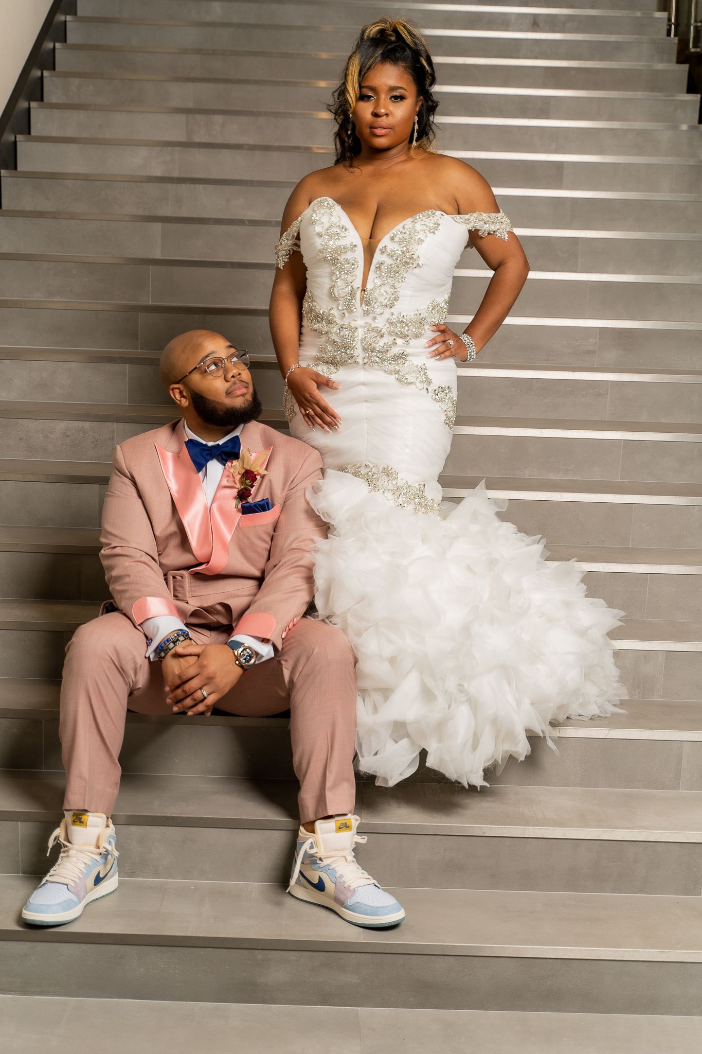 Fashion-forward wedding portrait on stairs with modern suit and dramatic mermaid gown.