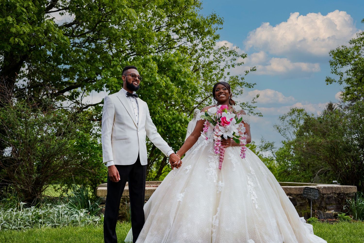 Wedding couple takes romantic photos in garden setting with blue sky backdrop.
