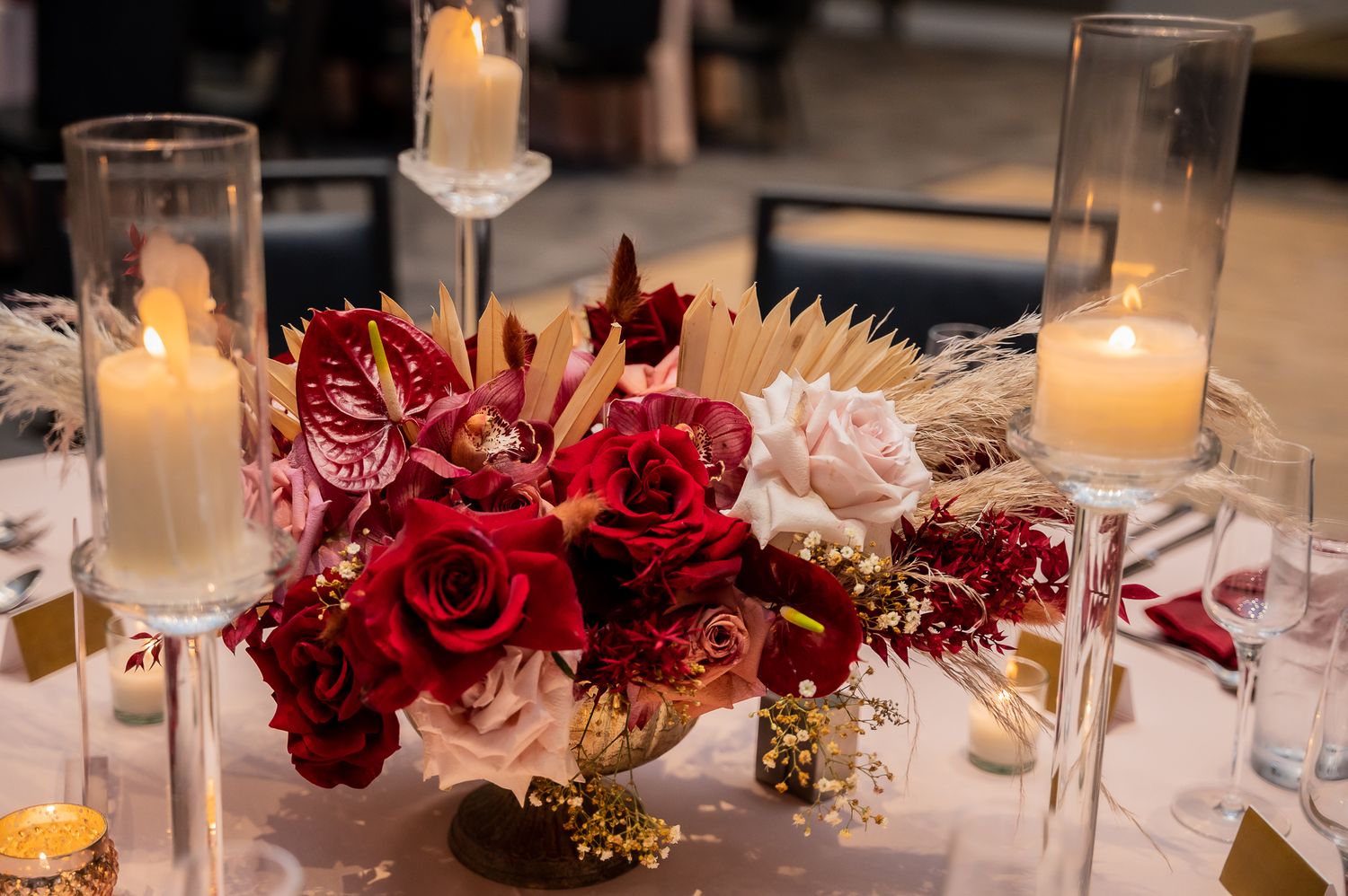 Elegant wedding centerpiece with deep red roses, burgundy florals and glowing candles on a formal table setting.