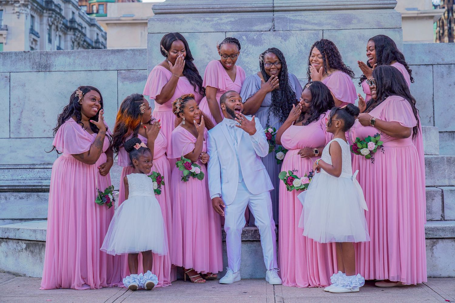 Wedding party poses on stone steps wearing pink bridesmaid dresses and white attire.