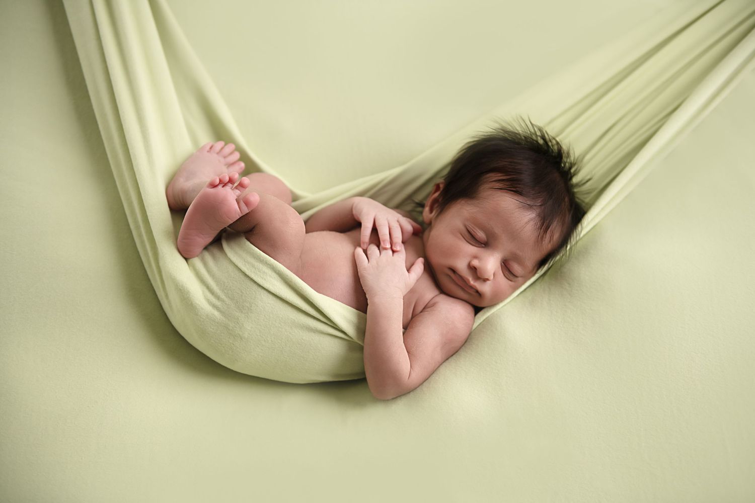 Sleeping newborn wrapped in soft cream fabric during studio portrait session.