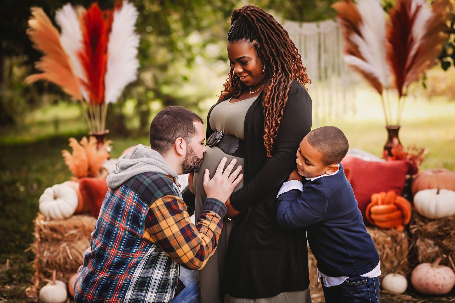 Family of 3 at fall maternity session with dad kissing mom's belly