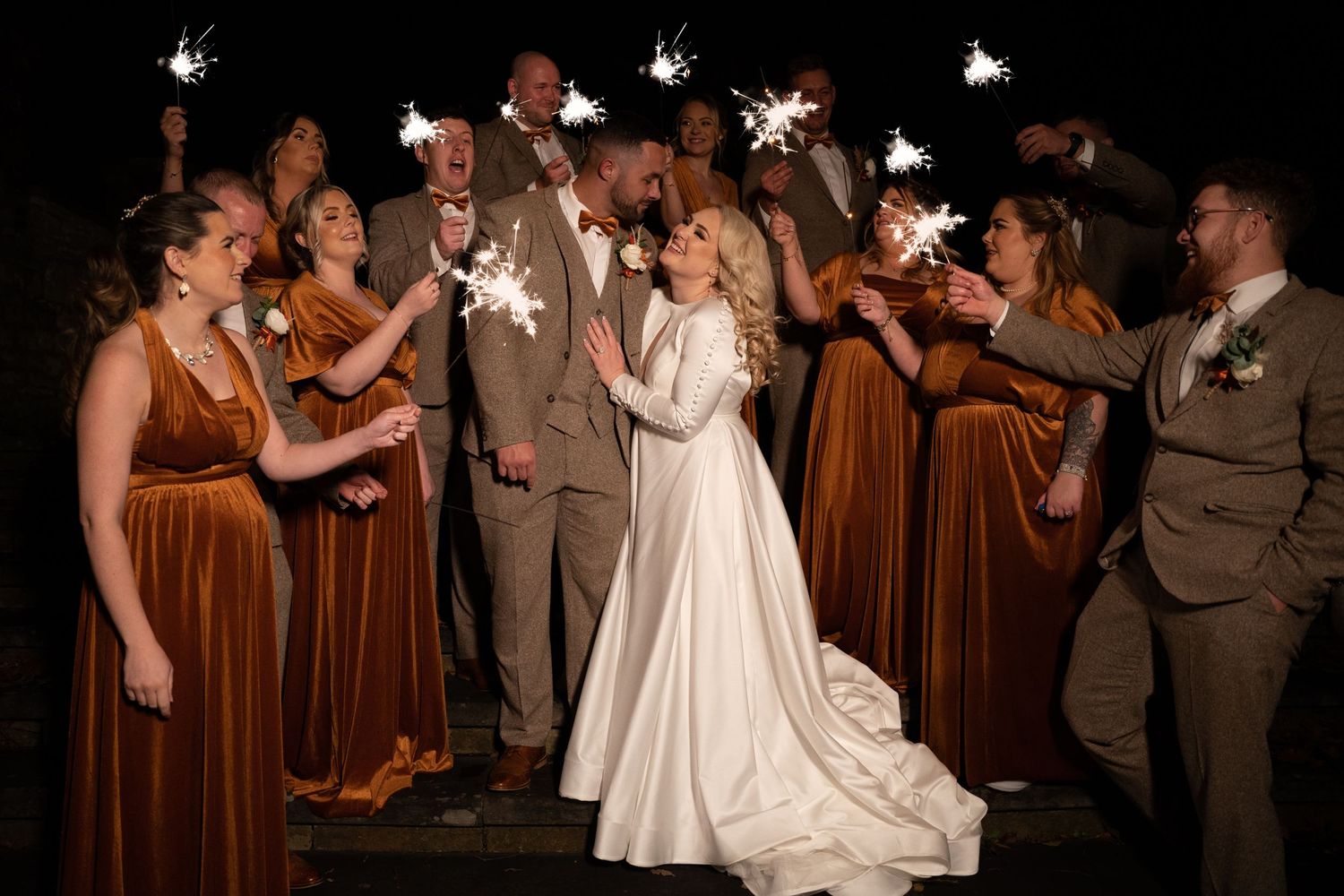 Wedding party stands together at night holding sparklers during a romantic sendoff celebration.
