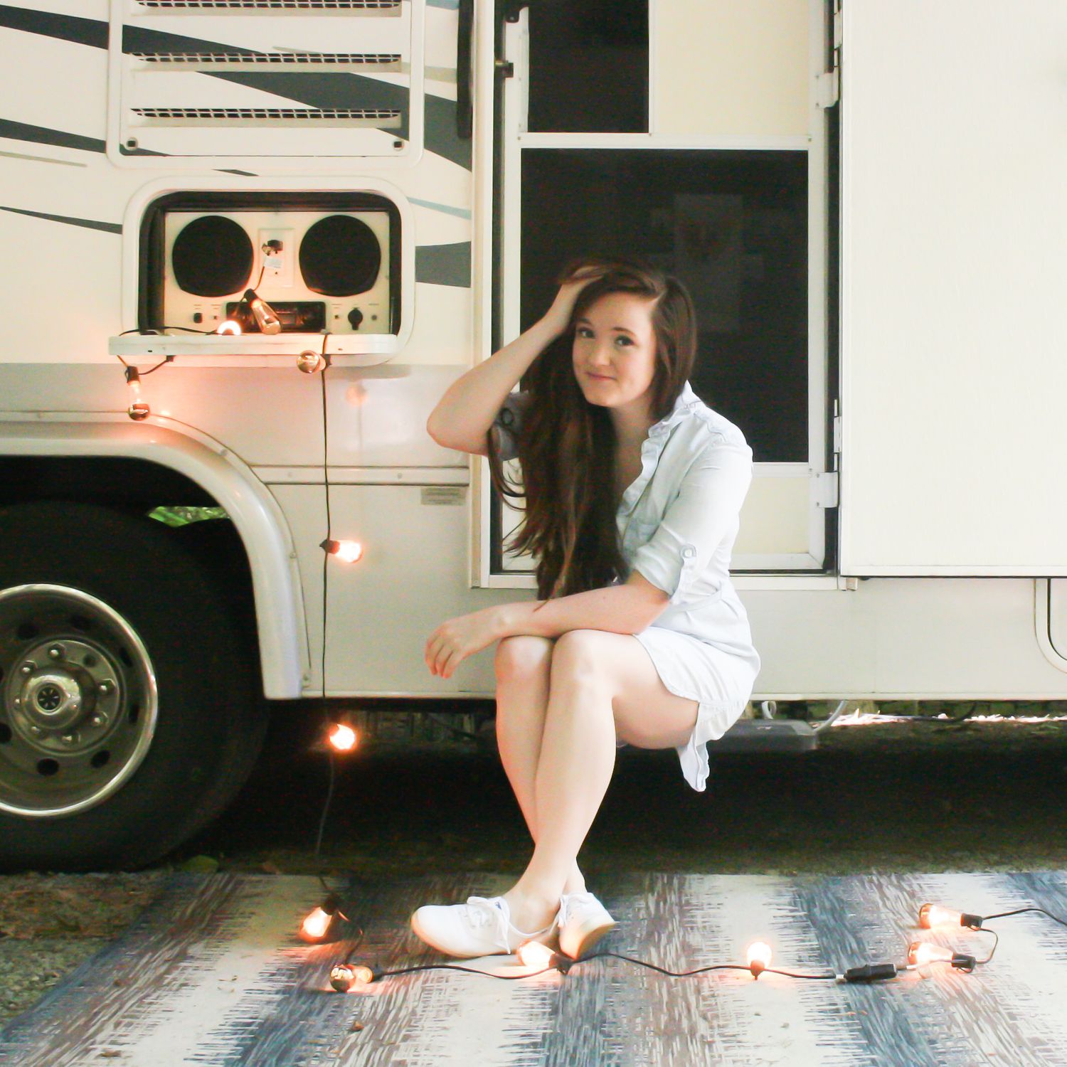 young woman sitting on camper steps with string lights