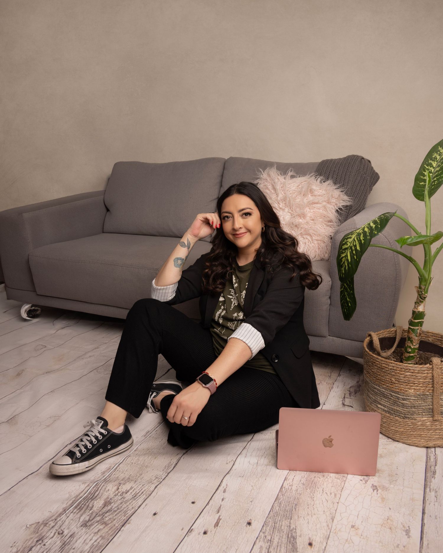 Casual home office setup with grey couch, rose gold laptop, and potted plant in cozy setting.