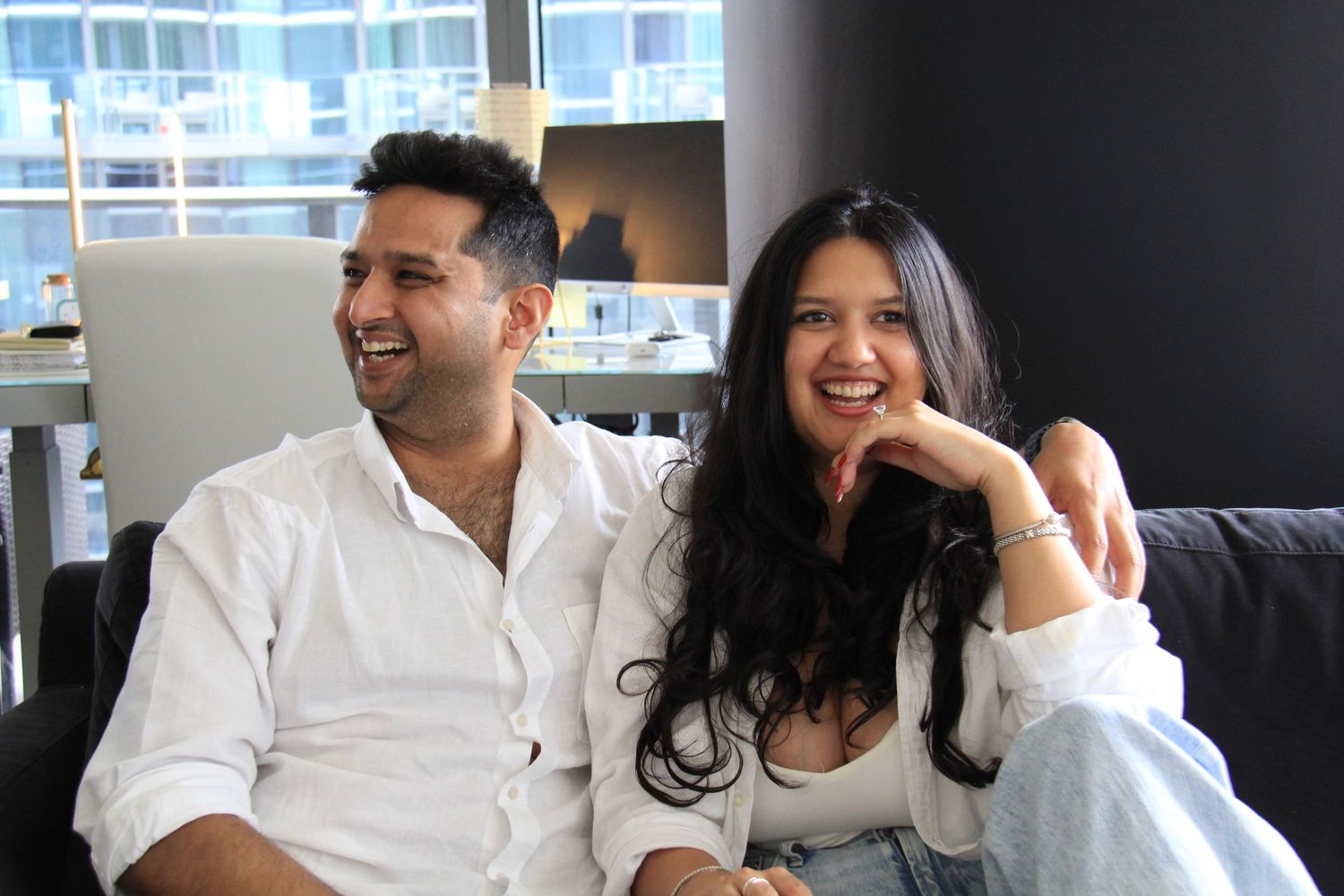 Two people share genuine laughter while relaxing on a modern gray couch.
