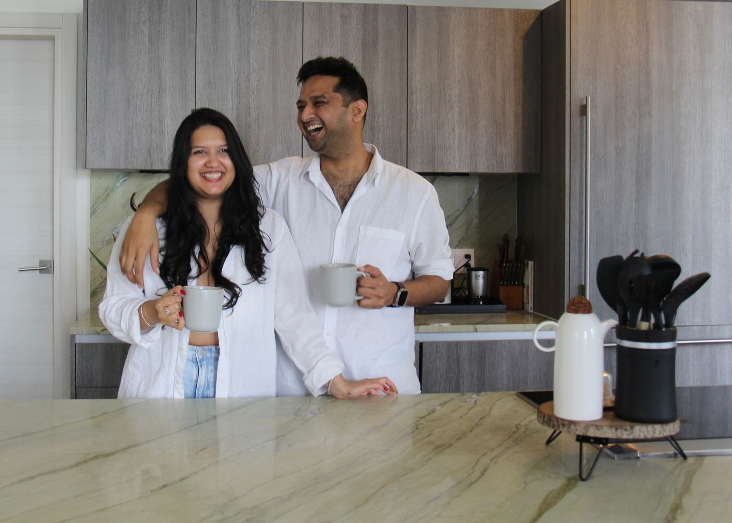 A couple enjoys their morning coffee together in a modern kitchen with wooden cabinets and white decor.