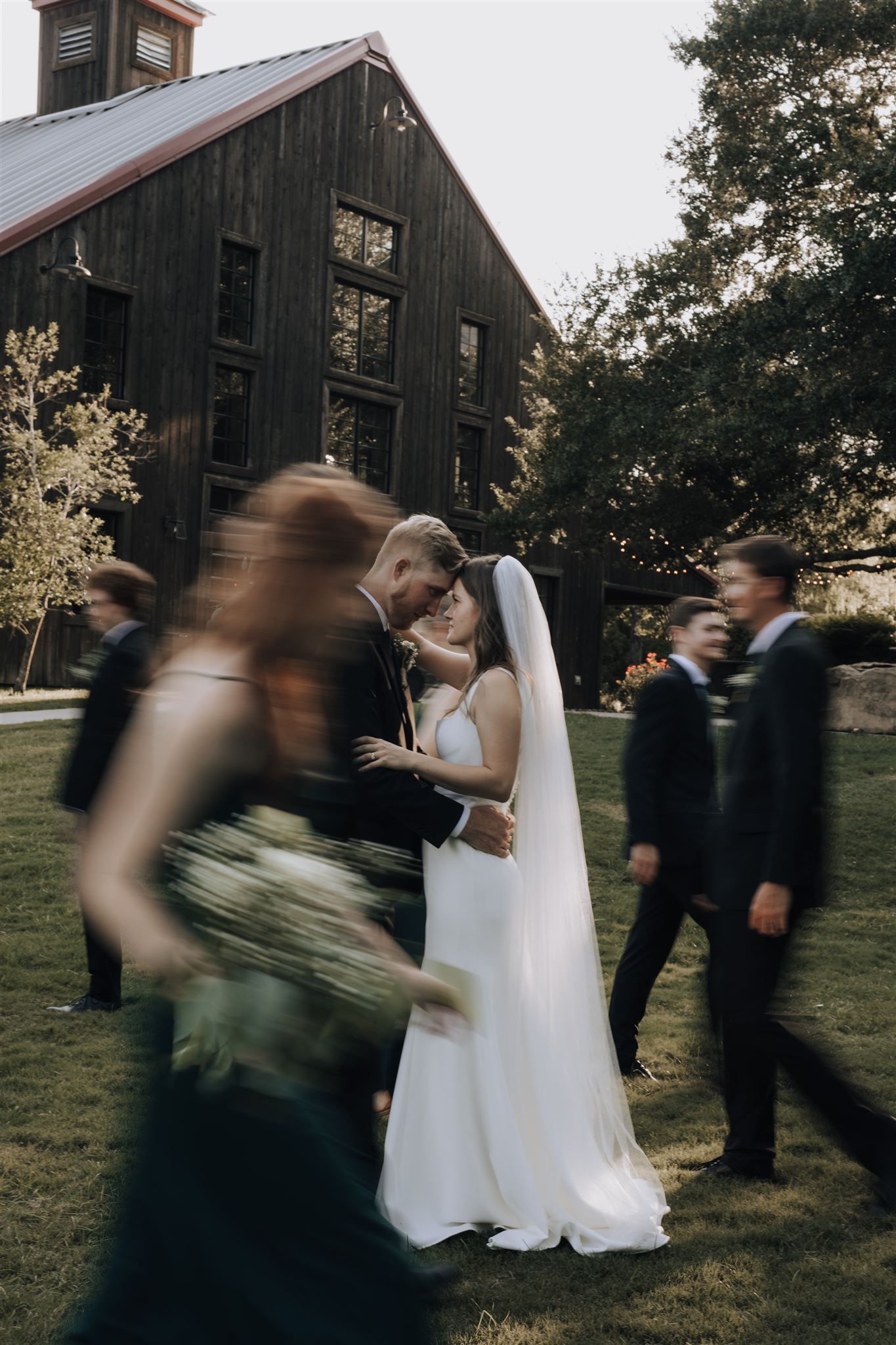 Wedding party in motion against rustic barn backdrop with artistic blur effect.