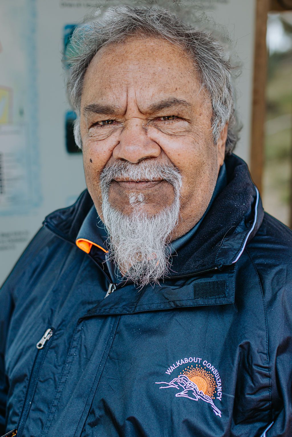 Person wearing navy jacket with embroidered logo smiles warmly during outdoor presentation.