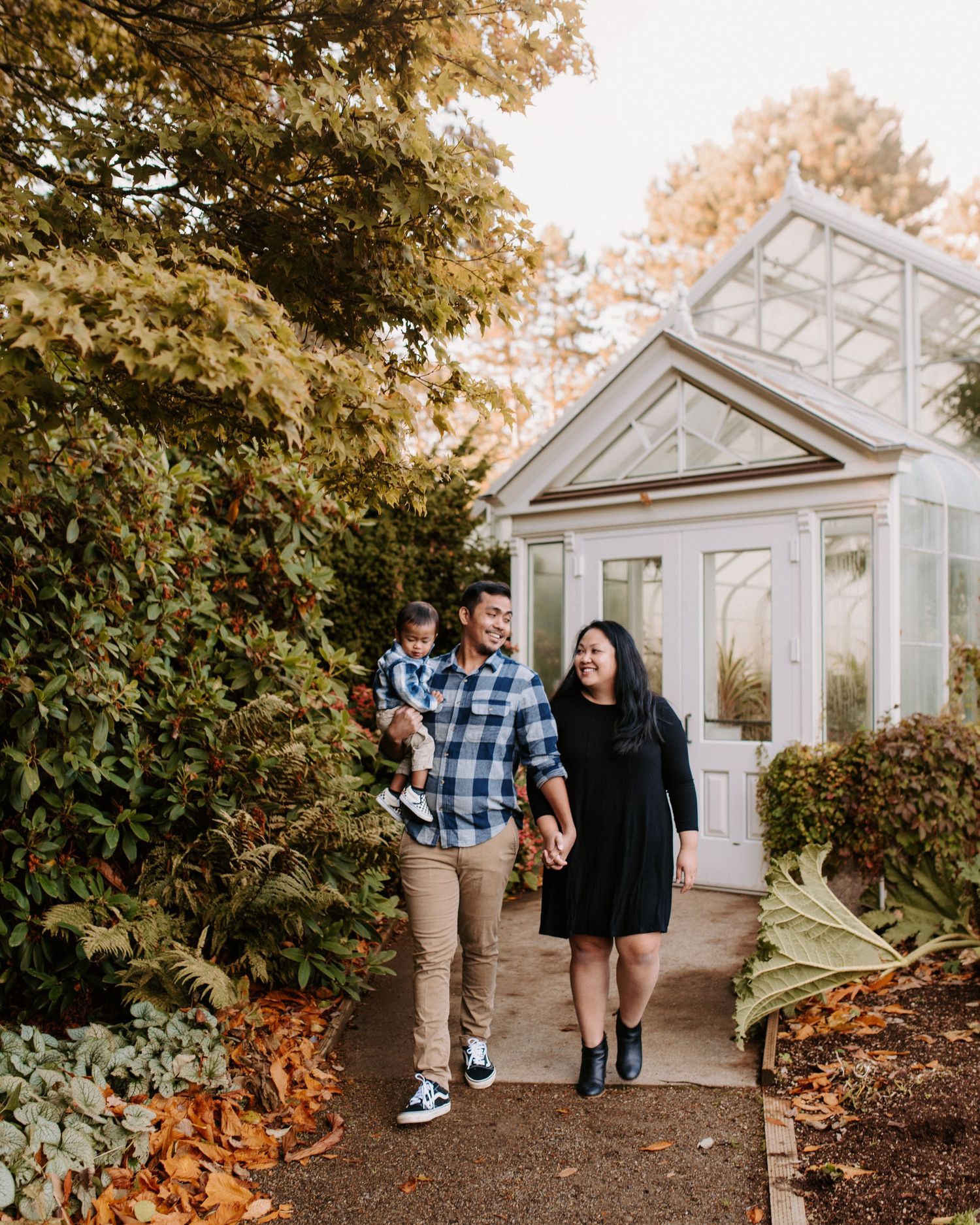 Couple strolls along garden path next to a white greenhouse structure.