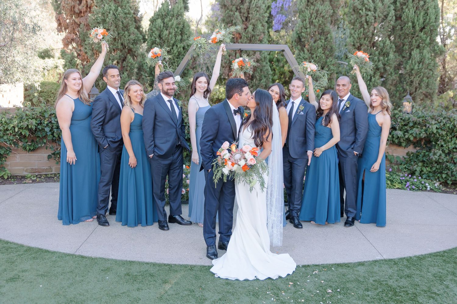 Bride and groom kissing outdoors with bridal party cheering