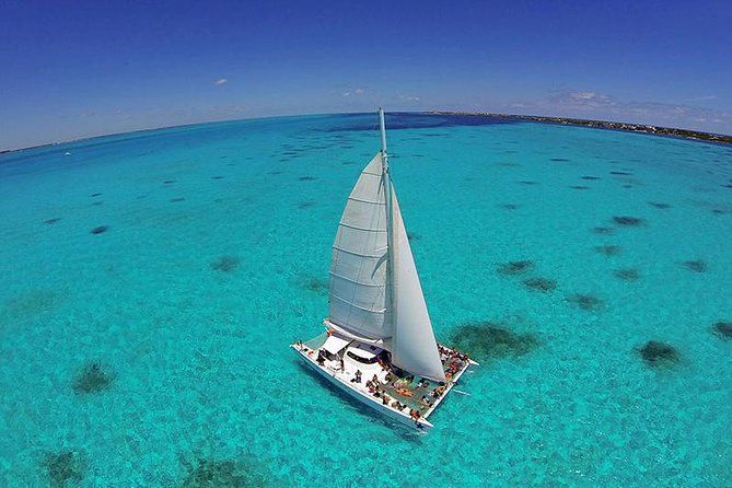 Aerial view of a white sailboat cruising through crystal clear turquoise waters in a tropical paradise.