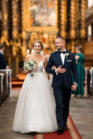 Wedding couple walks down church aisle with ornate golden decor.