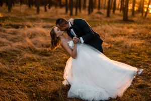 Romantic sunset wedding portrait in golden forest with dramatic dip pose.