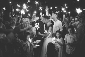 Wedding couple surrounded by guests holding sparklers during nighttime celebration.